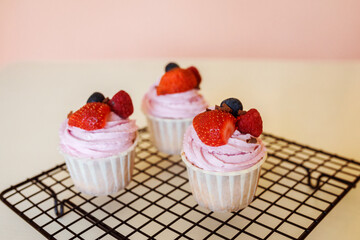 Appetizing cupcakes covered with pink whipped cream and fresh berries.