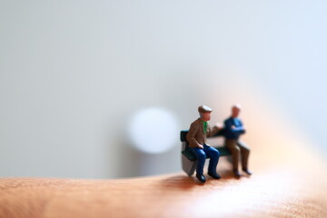 Miniature people on a bench, on the fence of a lobby. Having safe elder ages, retirement, life third era.