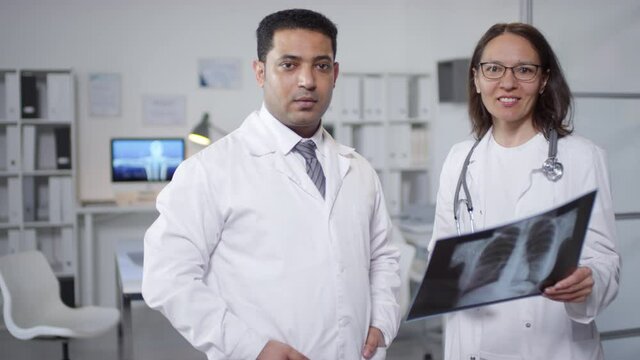 Medium portrait of professional pulmonologists standing together in doctors office, working with X-ray picture then looking at camera