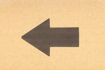 Black arrow pointing left on brown cardboard background