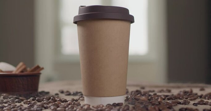 Paper cup for coffee or tea. A glass for take ava with latte or cabbage stands on the kitchen table with coffee beans in a beautiful composition. Cinematic slow motion in 4K.