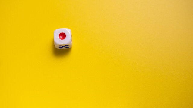 White dice with round dot number one on yellow background close-up. Concept of gambling and chance