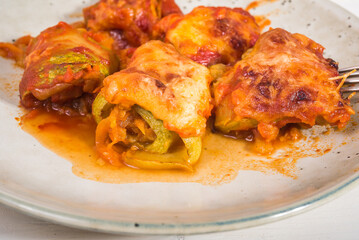 Zucchini rolls with vegetable filling baked with cheese in a plate on the kitchen table close-up