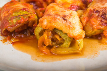 Zucchini rolls with vegetable filling baked with cheese in a plate on the kitchen table close-up