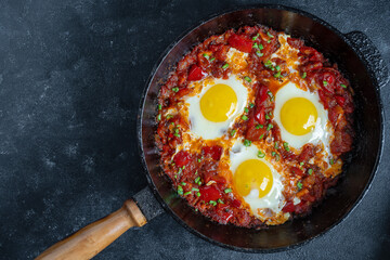 Shakshuka, fried eggs with tomatoes, onion, red pepper and spices in cast iron pan