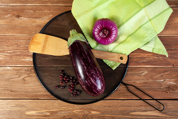 an aubergine, onion, wooden cooking spatula, haricot beans, black cover and green towel on brown wooden background