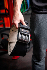 Sports leather black belt in the hand of a weightlifter