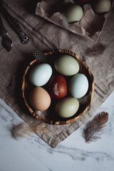 colorful chicken eggs lie in a wooden plate surrounded by feathers