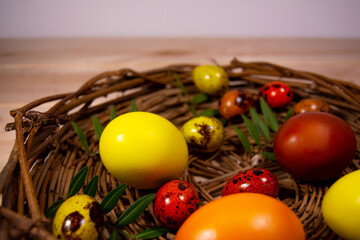 Eggs painted yellow, orange and brown lie in a nest made of wooden twigs on wooden table. The eggs...