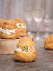 A traditional French savory choux dough cheese puff filled with fresh cheese, smoked salmon, dill leaf. Glass of champagne in background. Pastry most likely coming from burgundy serve as an appetizer 