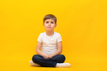 Little boy in jeans and a white t-shirt sits on an isolated yellow background