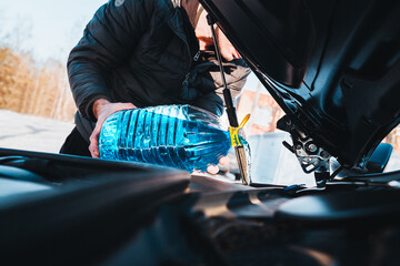 A man pours blue antifreeze liquid from a can into a car washer tank - winter maintenance