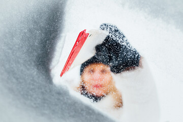 plastic ice scraper - a woman cleans the glass of a car in winter from snow