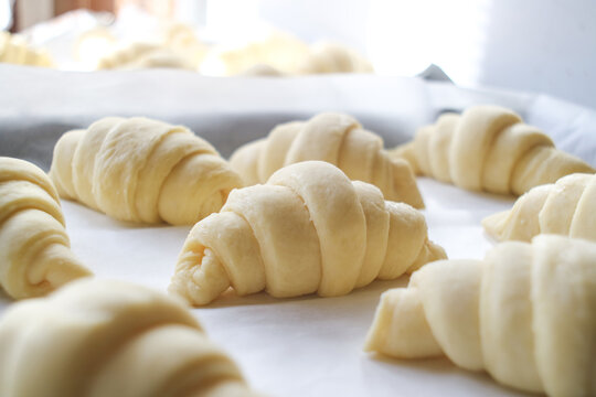Close up of layered of a fluffy leavened uncooked traditional French croissants dough roll in a baking tray&paper sheet, preparing to cook in oven. It's a buttery,flaky, pastry of Austrian origin