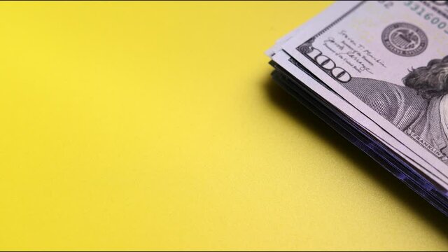Increasing stack of fiat money with face value of one hundred US dollars on yellow surface. Space for text. Concept of profit, successful investment. Stop motion shooting
