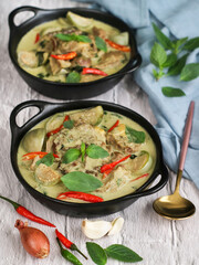 Bowls of traditional Thai green curry with lamb,eggplant&its ingredients and spices: grain de coriander, garlic, shallot, red chili and basilic leaves.The flavor base is curry paste and coconut milk