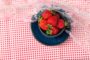 Beautiful and sweet strawberries in a ceramic cup on a red and white checkered tablecloth. Organic garden berries on the table