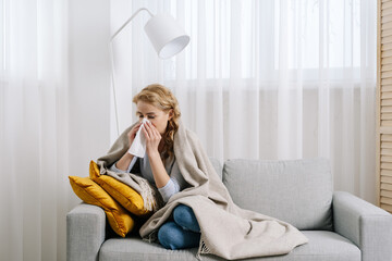 Sick woman covered with plaid sit on sofa