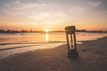 Hourglass on sand beach with sunset sky background.