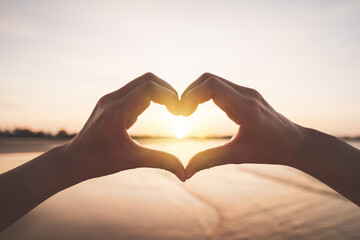 Female hands heart shape on nature bokeh sun light flare wave and blur tropical beach abstract...