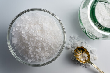 Glass jar and bowl of sea salt on white background