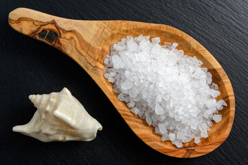Sea salt in wooden spoon and sea shell on black background