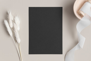 Black invitation card mockup with a lagurus on the beige table. 5x7 ratio, similar to A6, A5.