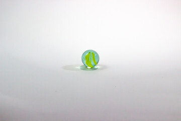 Close-up image of a green, yellow and blue colored marble ball isolated on a white background. Nostalgic toy. Selective focus.