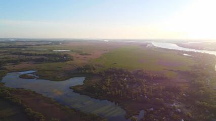 Drone fly over waving river of blue color surrounded by local village with various buildings and Wetland and marsh habitat with a reedbed of Common Reed aerial view.