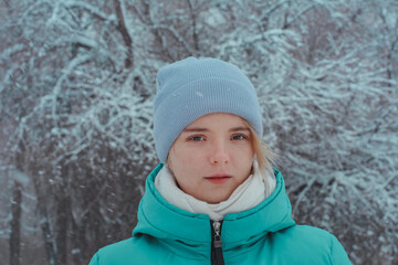 Portrait of a beautiful teenage girl 15 years old with brown eyes. Background of tree branches in hoarfrost and snowfall