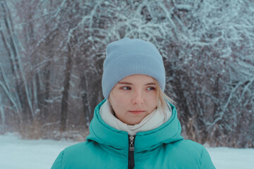 Fototapeta na wymiar Teenager girl in park in winter looks to side. Background of beautiful tree branches in hoarfrost and snowfall