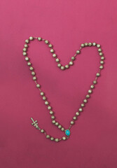 religious rosary with pearl and silver beads set in the shape of a heart on a fuchsia pink background