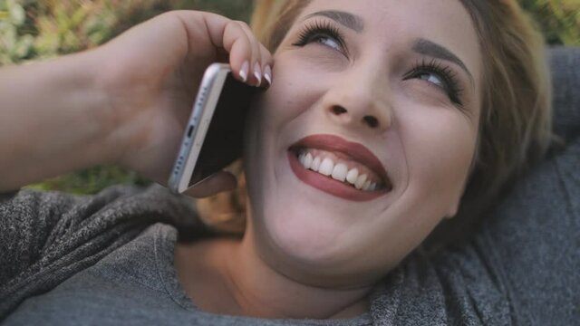 Sexy woman plus size speak mobile closeup. Body positive model talking phone at park. Sun nature landscape. Happy girl smiling, lay on green grass. Joyful vacation for recreation. Natural beauty