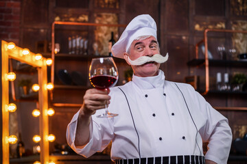 An elderly male chef degustation red wine in the kitchen