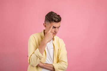 Fototapeta na wymiar Young man thinking . Handsome man in casual clothes is pointing away, looking at camera and smiling, on pink background