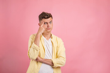 Fototapeta premium Young man thinking . Handsome man in casual clothes is pointing away, looking at camera and smiling, on pink background