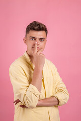 Young man thinking .  Handsome  man in casual clothes is pointing away, looking at camera and smiling, on pink background