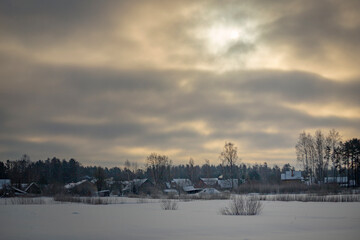 Latvian village in winter covered snow. White landscape Winter landscape in the Latvian village. Sunny day in the village. Roof covered with frost and icy white snow, cloudy sky in the foreground. 