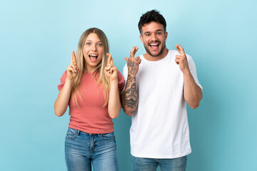 Young caucasian couple isolated on blue background with fingers crossing