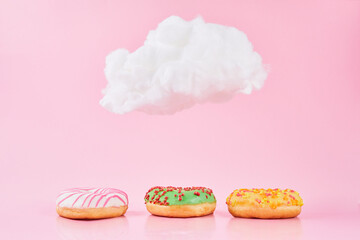 Sweet donuts with sprinkel and milk under a small cloud on a pink background. Various decorated...
