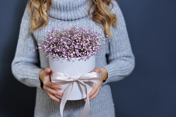 happy young blonde girl in a light gray sweater holds a bouquet of flowers in her hands on a dark gray monochrome background.