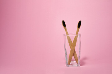 Eco friendly toothbrushes, zero waste concept. Natural bamboo toothbrush in glass jar on pink color background.