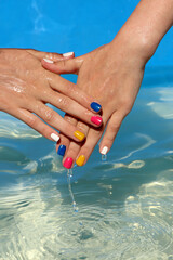 Children's hands with multicolored manicure are played with water.