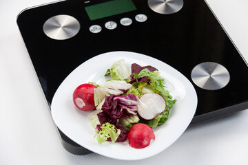 some salad on white plate standing on black scales on white background