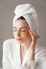Pretty european girl applying golden collagen patches under her eyes. Woman facial treatment. Cosmetology, beauty and spa.