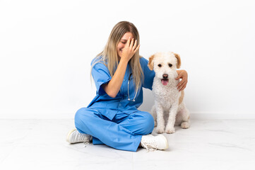 Young veterinarian woman with dog sitting on the floor laughing