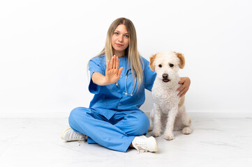 Young veterinarian woman with dog sitting on the floor making stop gesture