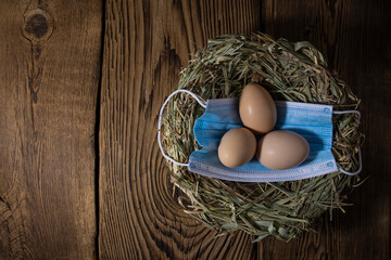 eggs in a nest of straw with a medical mask on vintage wood background with copy space, easter quarantine concept.