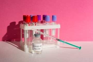 Covid 19 vaccine bottle and syringe on a pink background.