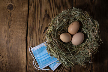 eggs in a nest of straw with a medical mask on vintage wood background with copy space, easter quarantine concept.
